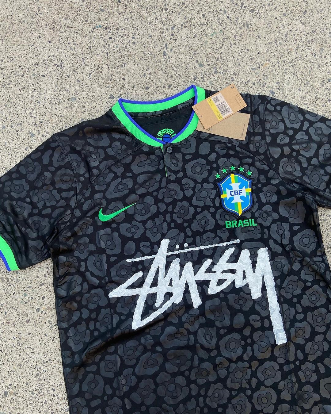 Close-up of a black Brazil x Stussy soccer jersey. The collar features a green and blue stripe with the Nike and CBF logos. 